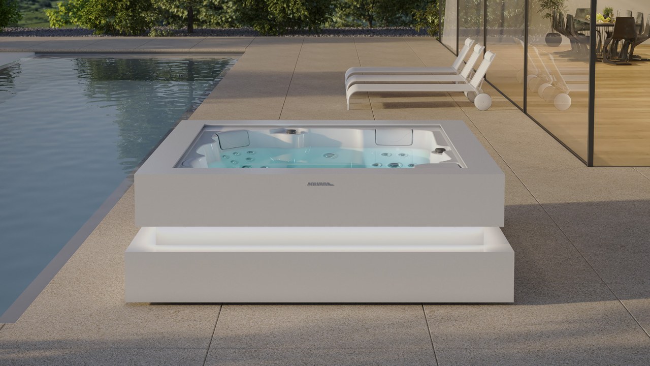 Spa Cube Ergo en blanco con base iluminada junto a alberca y camastros